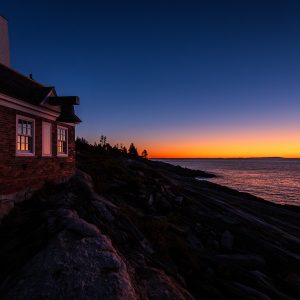 Predawn light glows orange over the Atlantic Ocean beside Pemaquid Point Lighthouse in Bristol, Maine.