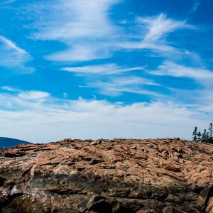 Granite ledges at Schoodic Point in Acadia National Park, Maine, beneath a bright blue summer sky with wispy clouds.