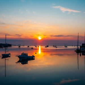 Sunrise over Rockland Harbor, Maine, with boats reflected in calm golden water.