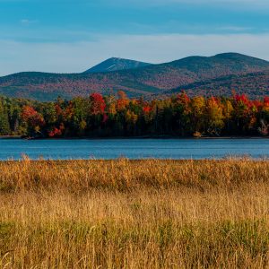 Flagstaff Lake in Western Maine surrounded by autumn color and backed by Sugarloaf Mountain under clear blue skies.