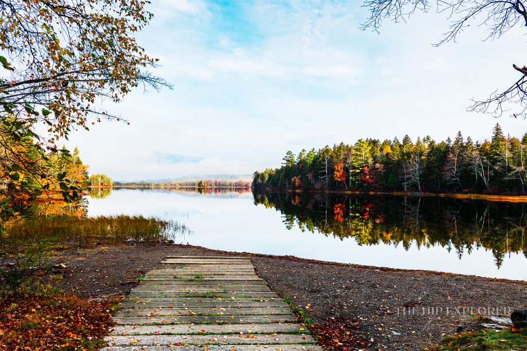 Cement boat landing leading into a calm lake surrounded by colorful autumn trees in Northport, Maine.