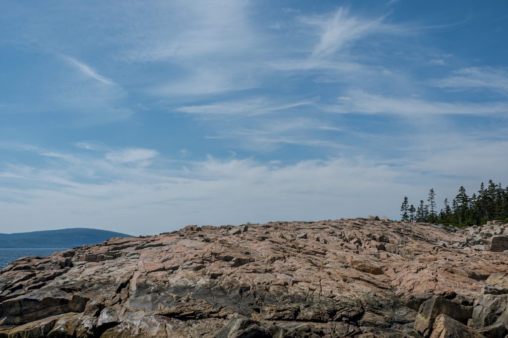 Expansive granite rock formations at Schoodic Point beneath a soft blue summer sky in Maine.
