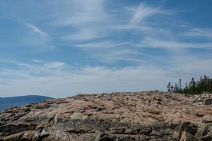 Expansive granite rock formations at Schoodic Point beneath a soft blue summer sky in Maine.