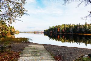 Cement boat landing leading into a calm lake surrounded by colorful autumn trees in Northport, Maine.
