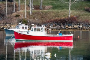 A bright red fishing boat anchored in Rockport Harbor with its reflection shimmering on calm water.