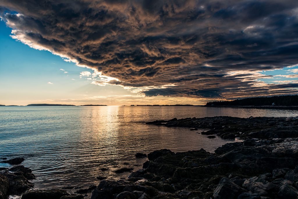 Dramatic storm clouds sweeping over the coast near Marshall Point at sunset, with warm evening light reflecting across calm water.