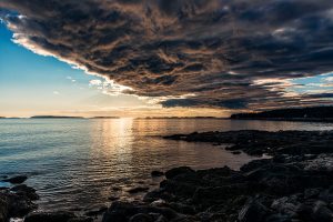 Dramatic storm clouds sweeping over the coast near Marshall Point at sunset, with warm evening light reflecting across calm water.