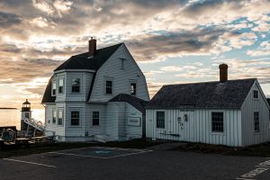 Keeper’s house and museum buildings at Marshall Point Lighthouse under dramatic late-afternoon clouds.