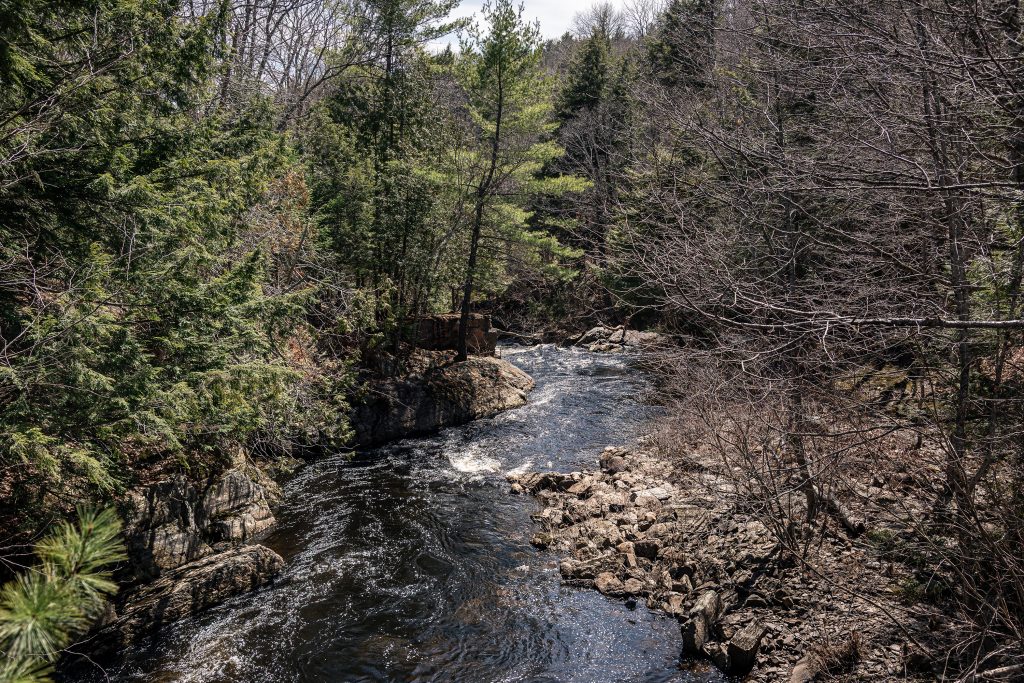Curving river through wooded landscape at Monroe Falls Maine with rocks, trees, and flowing water in early spring.