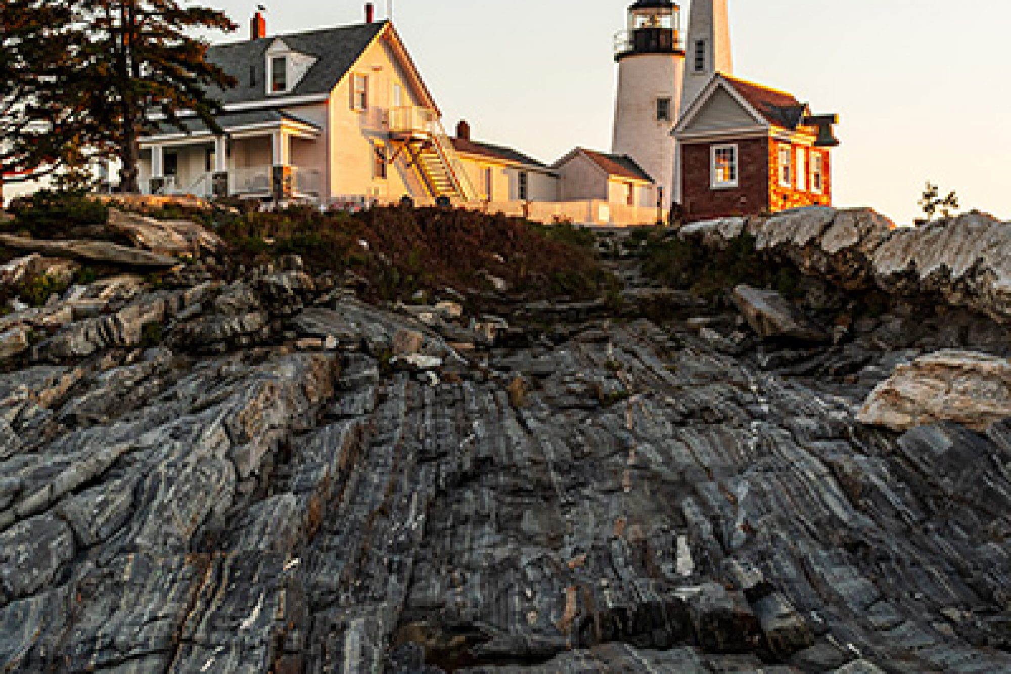 Reflection of Pemaquid Point Lighthouse in a tide pool among rocky coastal cliffs at sunset in Bristol, Maine.