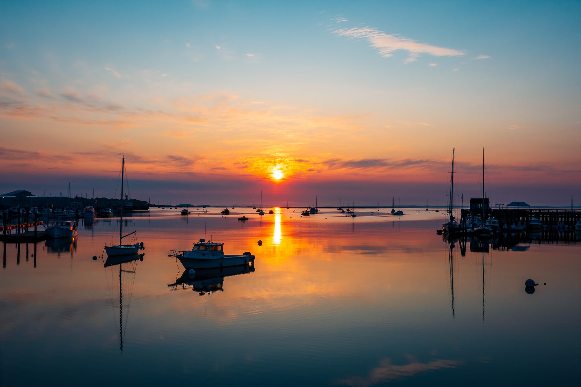 Sunrise over Rockland Harbor, Maine, with boats reflected in calm golden water.