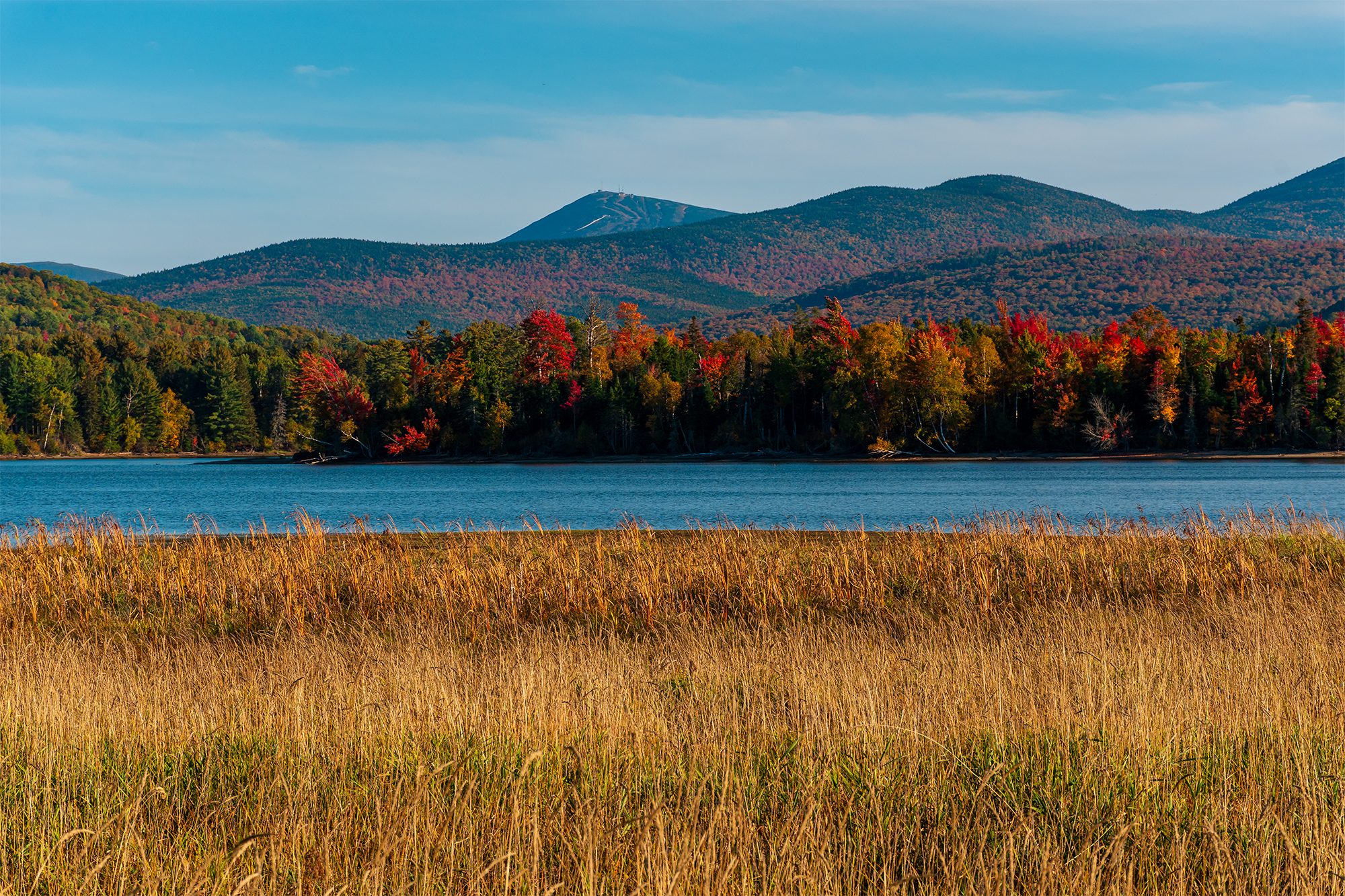 Flagstaff Lake in Western Maine surrounded by autumn color and backed by Sugarloaf Mountain under clear blue skies.