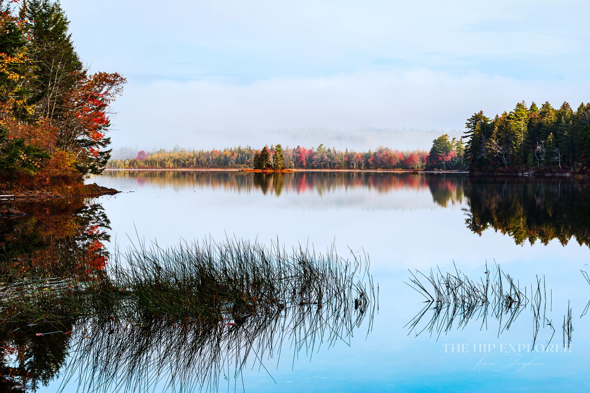 A foggy autumn morning in Northport, Maine, with colorful trees reflected in calm lake water.