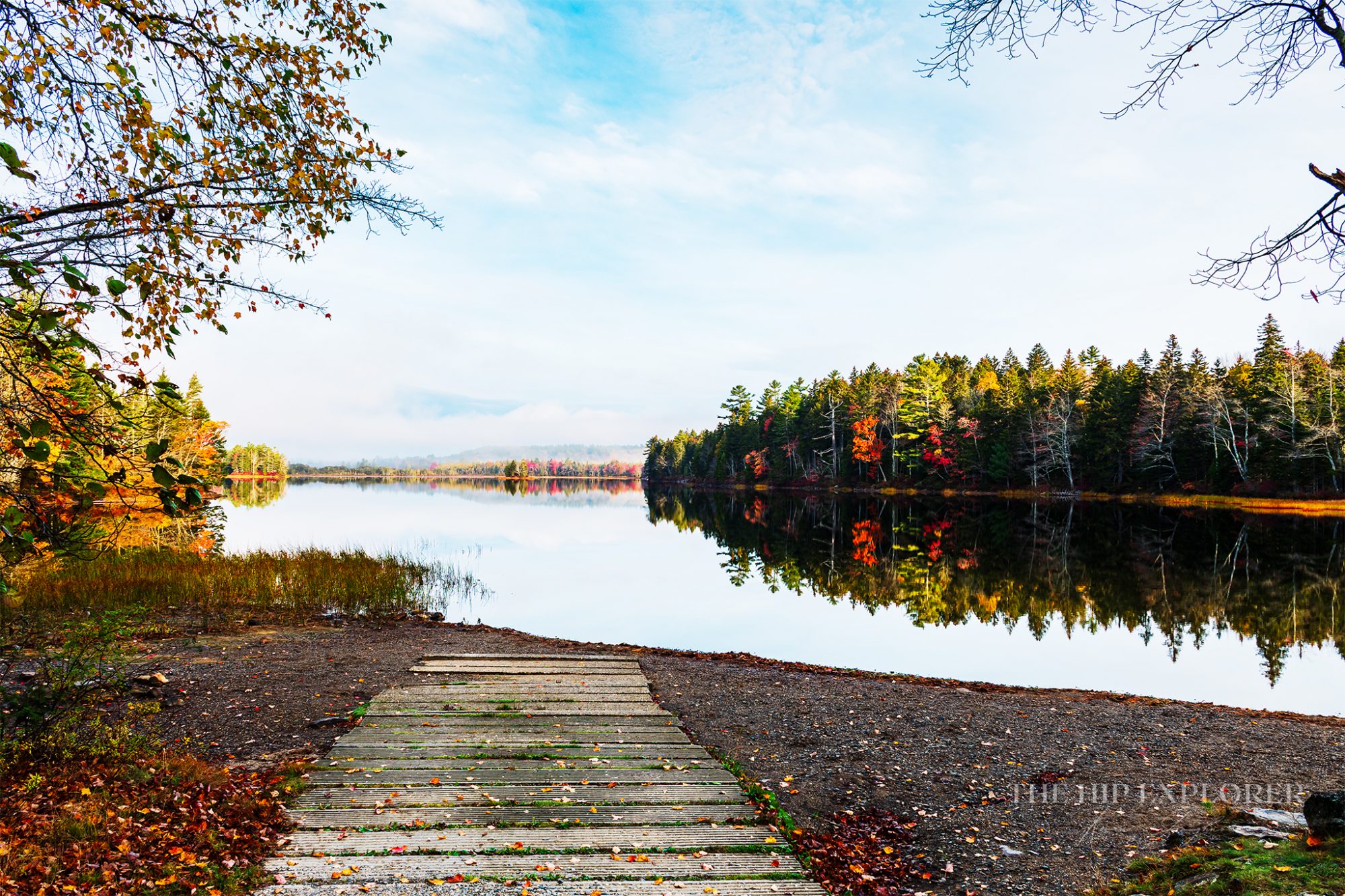 Cement boat landing leading into a calm lake surrounded by colorful autumn trees in Northport, Maine.